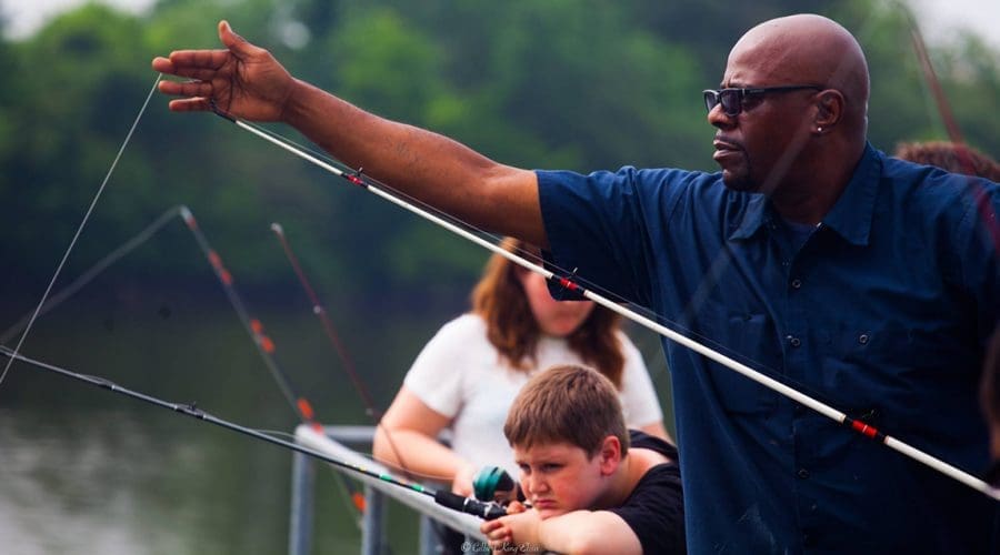 A man in a blue shirt checking the line on his fishing rod while others fish in the background
